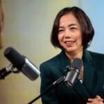 Fei-Fei Li speaking at a conference, with a cityscape in the background.