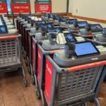 A Caper AI shopping cart with a digital screen displaying product information in a grocery store aisle.