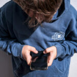 صورة لشاب يلعب على هاتفه المحمول فيما يظهر خلفية لمنصة تواصل اجتماعي.