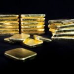 قضبان ذهبية لامعة مع رسم بياني يظهر انخفاضاً في الأسعار، تعكس تراجع قيمة المعدن النفيس عالمياً.