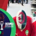 صورة للمنتخب المغربي يحتفل بفوز في كأس إفريقيا، مع خلفية تظهر معالم مغربية متنوعة.