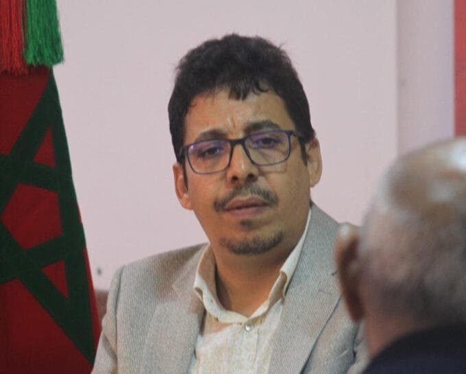 وصف الصورة بالإنجليزية: صورة لشخص يرفع العلم الصحراوي مع خلفية للصحراء.