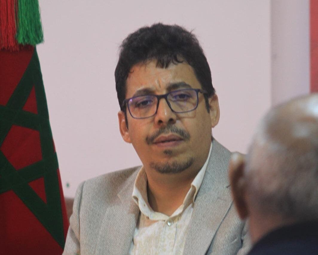 وصف الصورة بالإنجليزية: صورة لشخص يرفع العلم الصحراوي مع خلفية للصحراء.