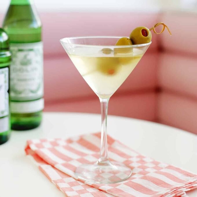 A perfectly chilled Dirty Martini garnished with three green olives on a cocktail pick, served in a classic stemmed martini glass.