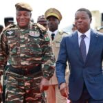 Un homme en train de discuter avec un autre homme, avec un paysage africain en arrière-plan.