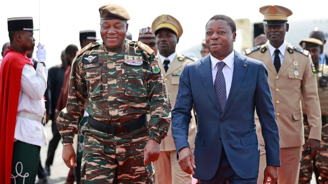 Un homme en train de discuter avec un autre homme, avec un paysage africain en arrière-plan.