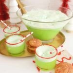 Vibrant green Grinch Punch with scoops of lime sherbet floating, garnished with a red sugar rim, in a festive punch bowl.
