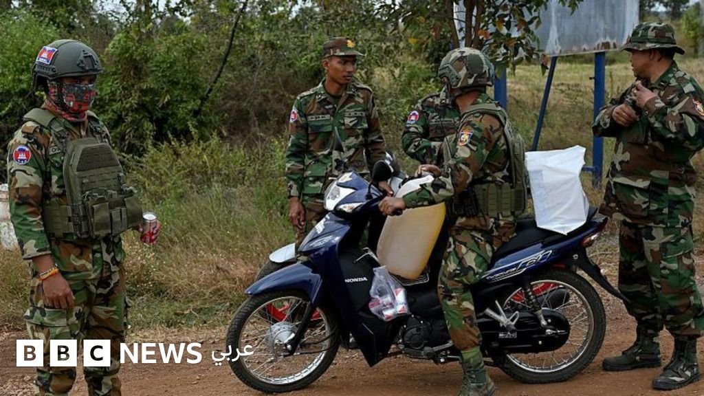 Un soldat thaïlandais se tient debout près d'une voiture de combat, avec un paysage de jungle en arrière-plan.