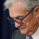 Donald Trump speaking at a podium with the Federal Reserve building in the background