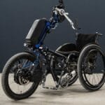 Un homme en fauteuil roulant pédalant sur un vélo électrique adapté.