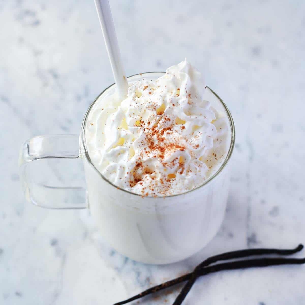 "A steaming mug of white hot chocolate topped with whipped cream and a sprinkle of cinnamon."