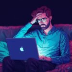 A person sitting alone at a kitchen table, looking at a phone screen with a thoughtful or weary expression, illuminated by the screen's glow.