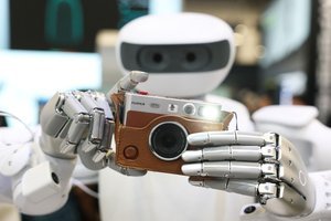 A robot wearing a cowboy hat at CES 2026, attempting to hand over an item, symbolizing AI's presence and occasional stumbles at the event.