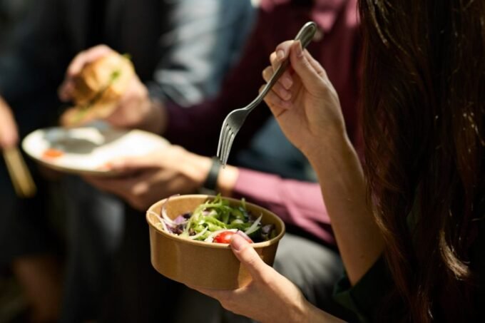 An AI robot hand offering a protein bar to a hesitant employee, symbolizing corporate control over personal choices.
