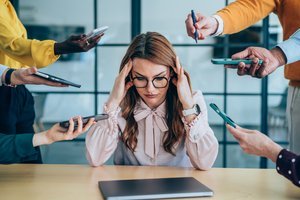 A person looking stressed at a desk while others enjoy vacation, symbolizing the reluctance to take time off.