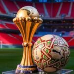 Le ballon officiel ITRI de la CAN 2025, de couleur dorée, posé sur un terrain de football, avec les logos de la CAF et Puma, symbolisant la finale Maroc-Sénégal.