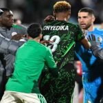 Scène de tension après un match de football, avec des joueurs entourant un arbitre et des forces de sécurité intervenant.