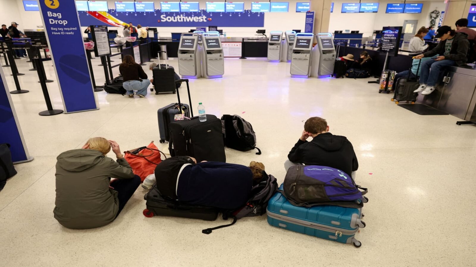 Caribbean Skies Reopen: Airlines Scramble After Venezuela Strikes Strand Thousands 3 Passengers resting on the floor at Luis Muñoz Marín International Airport after flights were delayed and canceled due to airspace closure.