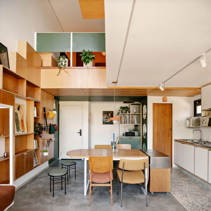 Interior view of Studio Papaya's SBC Apartment showing the open-plan living area with green entry, multi-functional table, and double-height window.