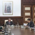 Le Chef du gouvernement Aziz Akhannouch présidant une réunion du Conseil de gouvernement, avec des documents et des ministres en arrière-plan, symbolisant les décisions et réformes à venir.