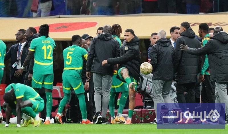 شعار الكونفدرالية الإفريقية لكرة القدم (الكاف) مع خلفية لملعب كرة قدم بعد مباراة متوترة.