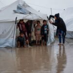 امرأة تصلح خيمتها بينما يقف أطفال في مخيم مؤقت للنازحين الفلسطينيين في حي الزيتون بغزة بعد أمطار غزيرة.