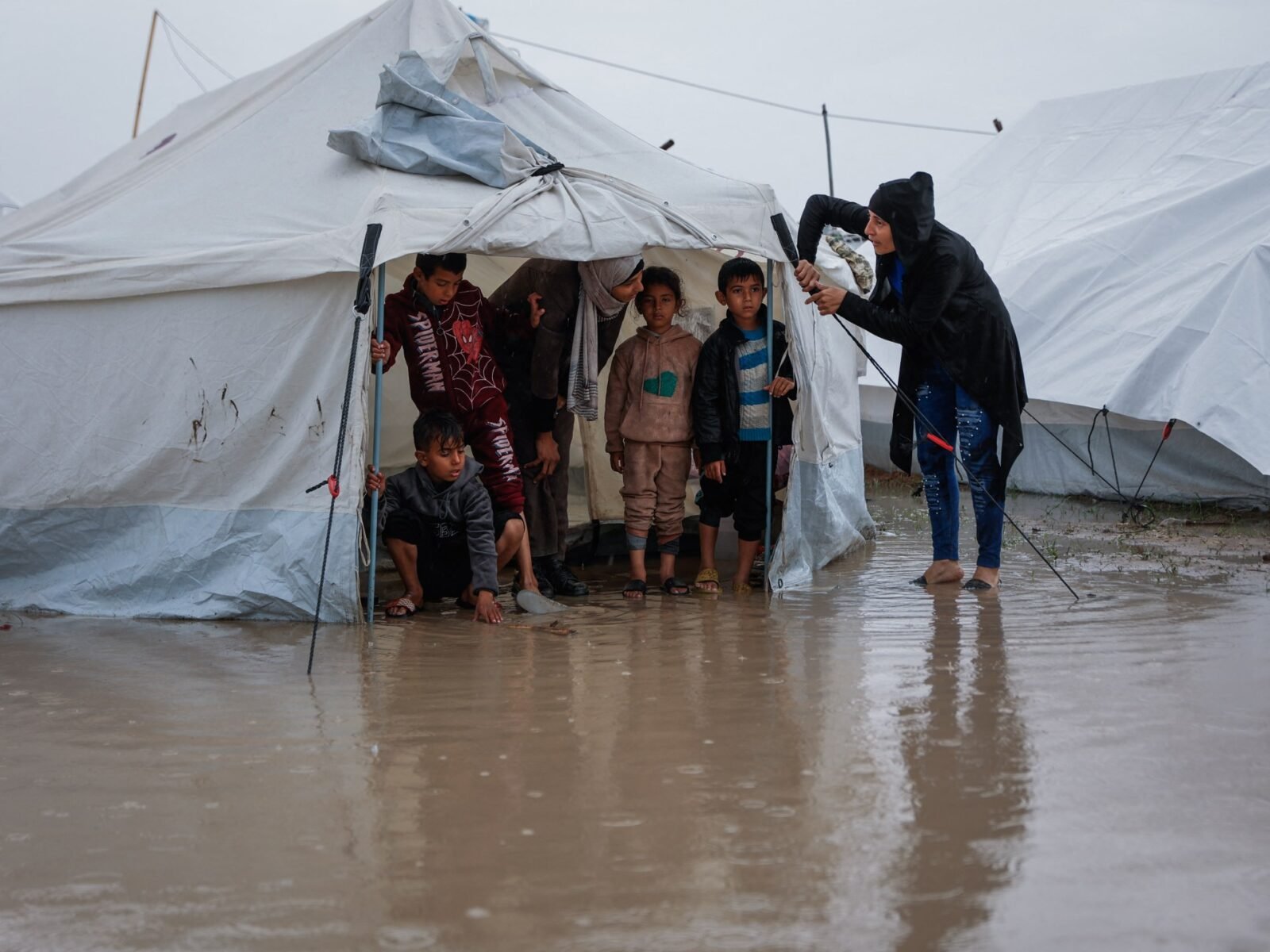 امرأة تصلح خيمتها بينما يقف أطفال في مخيم مؤقت للنازحين الفلسطينيين في حي الزيتون بغزة بعد أمطار غزيرة.