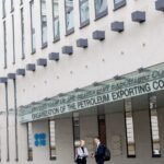 علم فنزويلا وخلفه منصات نفطية مع شعار أوبك+