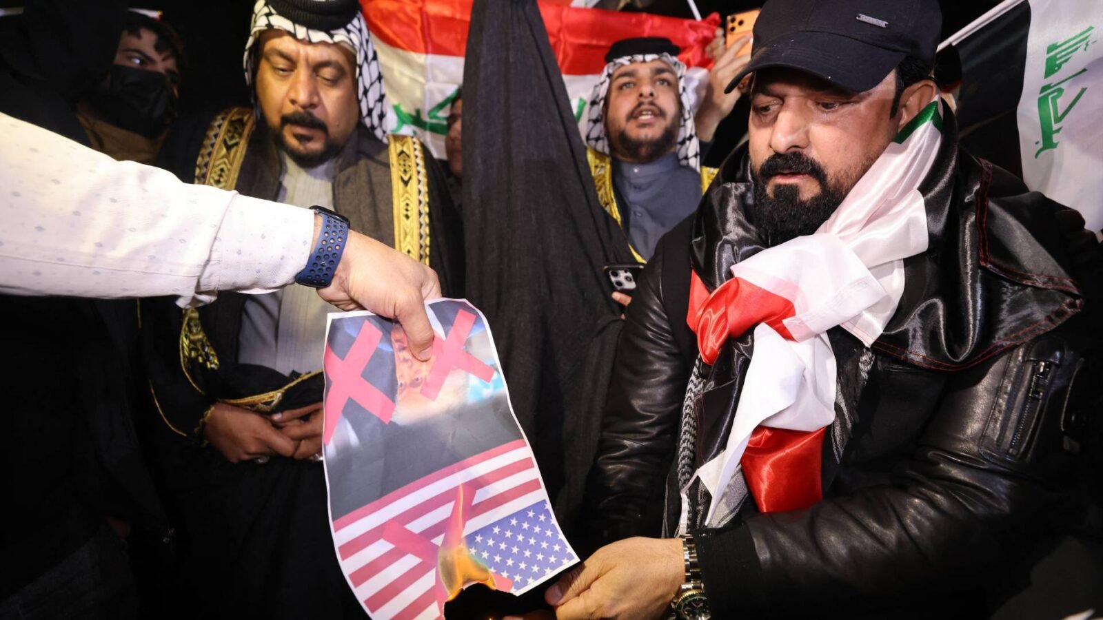 متظاهرون عراقيون يحرقون صورة للرئيس الأمريكي دونالد ترمب قرب السفارة الأمريكية في بغداد.