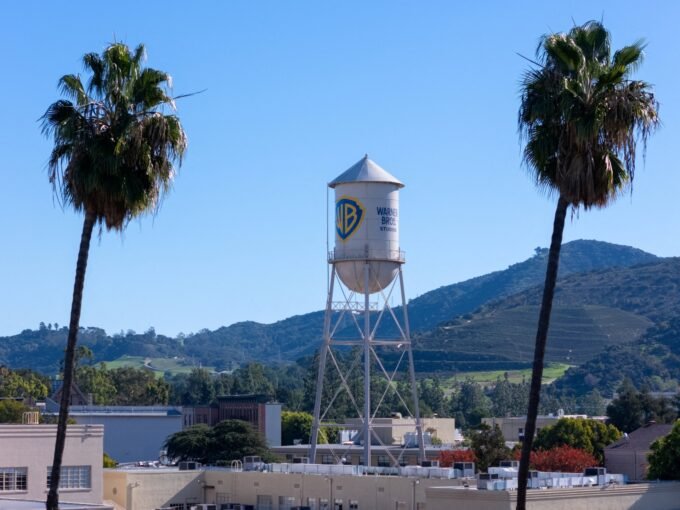 شعار وارنر براذرز ديسكفري مع خلفية تعبر عن صراع الاستحواذ بين الشركات الإعلامية الكبرى.