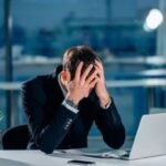 شخص مرهق يعمل في مكتب يمسك رأسه، يرمز للإرهاق الوظيفي والضغط النفسي.