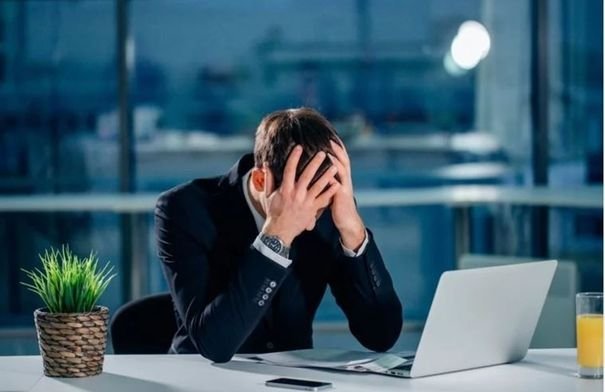 شخص مرهق يعمل في مكتب يمسك رأسه، يرمز للإرهاق الوظيفي والضغط النفسي.
