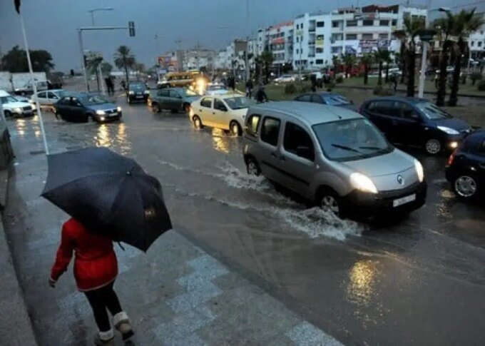 صورة توضيحية لسيارة تسير بحذر على طريق جبلي مغطى بالثلوج والأمطار، مع لافتات تحذيرية.