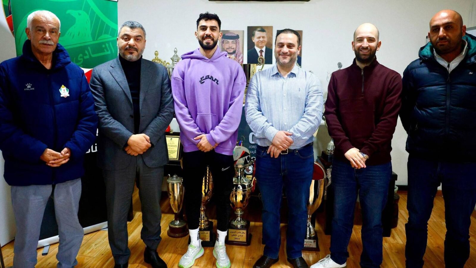 صورة تظهر رئيس نادي الوحدات يوسف الصقور ورئيس النادي الأهلي سمير صوبر وهما يصافحان اللاعب عبدالله عوض بعد توقيع عقد انتقاله.