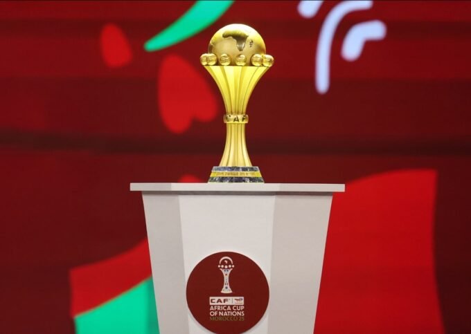 شعار كأس أمم إفريقيا 2025 في المغرب مع خلفية لملعب كرة قدم