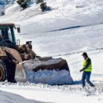 Vue aérienne d'un camion étrave déneigeant une route de montagne enneigée à Béni Mellal, sous un ciel nuageux, avec des sommets recouverts de neige en arrière-plan.