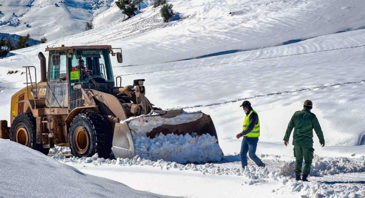 Béni Mellal : La Province Déploie un Dispositif Exceptionnel Face aux Chutes de Neige 3 Vue aérienne d'un camion étrave déneigeant une route de montagne enneigée à Béni Mellal, sous un ciel nuageux, avec des sommets recouverts de neige en arrière-plan.