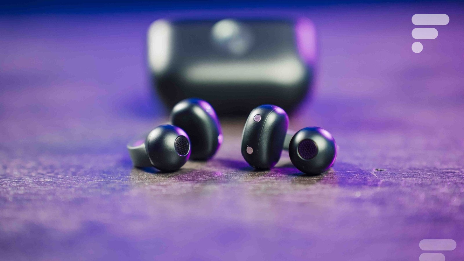 Les écouteurs Motorola Buds Loop noirs, avec leur design à clip d'oreille, posés sur une surface claire, illustrant leur forme ergonomique et compacte.