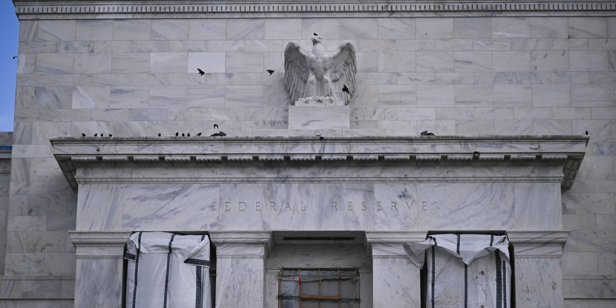 Federal Reserve Chairman Jerome Powell speaking at a press conference, with the US Capitol building in the background.