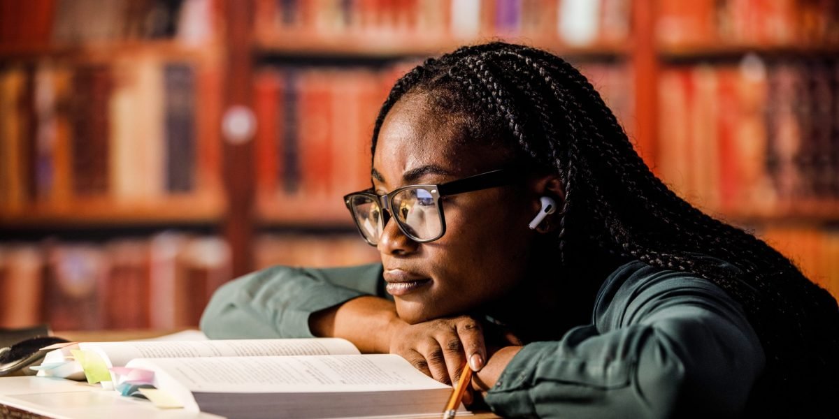 A young student looking perplexed at an open book in a college library, symbolizing the struggle with reading comprehension.
