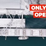 An aerial view of a remote mining operation in the icy, mountainous landscape of Greenland, with heavy machinery visible against the snow.