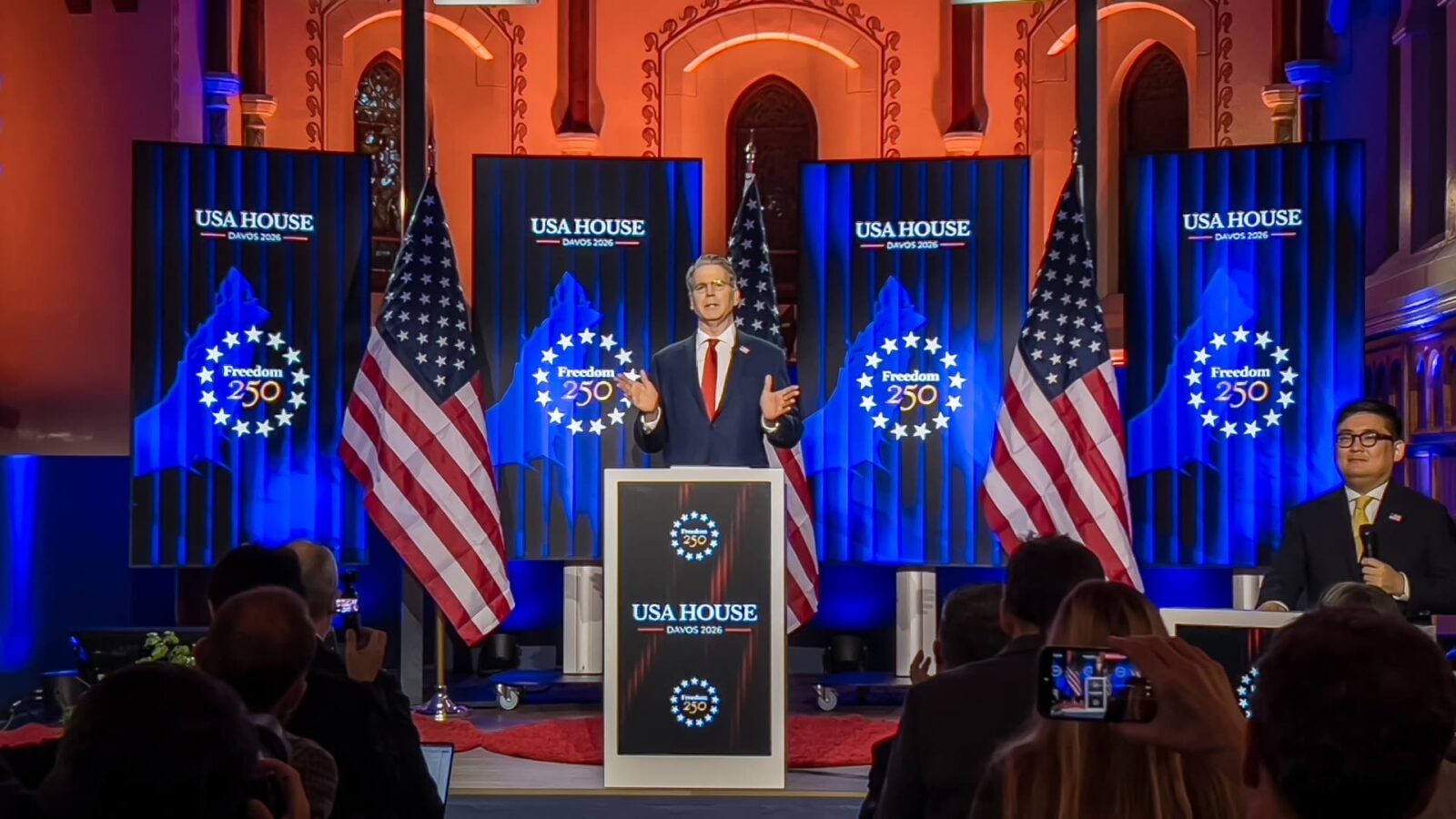 US Treasury Secretary Scott Bessent speaking at the World Economic Forum, with a map of Greenland in the background.