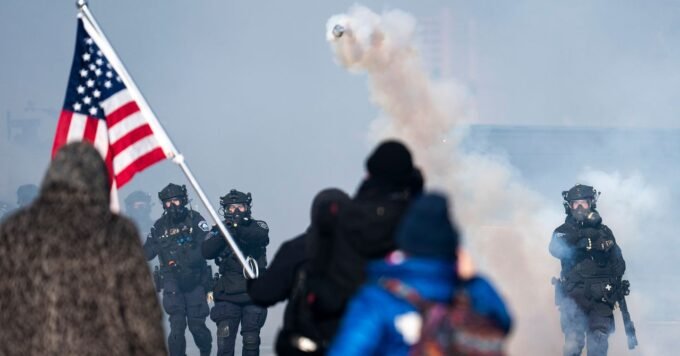 Federal immigration agents in tactical gear patrolling a street in Minneapolis, with local law enforcement visible in the background, symbolizing the tension between state and federal authority.