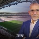 A perfectly green football pitch in a Moroccan stadium during heavy rain, with players in action, demonstrating effective drainage.