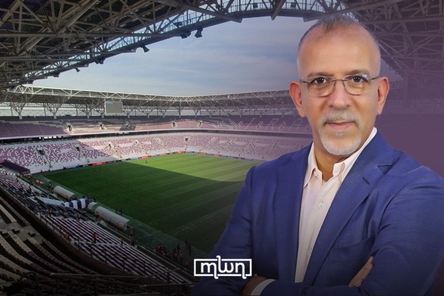 A perfectly green football pitch in a Moroccan stadium during heavy rain, with players in action, demonstrating effective drainage.
