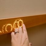 The Mui Board, a minimalist wooden smart home controller, mounted on a wall with glowing dot-matrix icons.