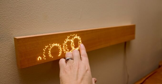 The Mui Board, a minimalist wooden smart home controller, mounted on a wall with glowing dot-matrix icons.