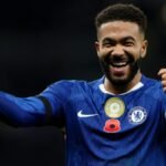 A football player in a blue jersey (Napoli) and a player in a white jersey (Chelsea) challenging for the ball during a Champions League match.