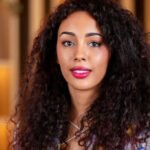 Une main humaine et une main robotique se touchant, symbolisant l'interaction entre l'humain et l'intelligence artificielle dans l'expérience client, avec un arrière-plan flou de la ville de Marrakech.