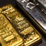 Gold and silver bars stacked next to a chart showing market volatility and price increases.